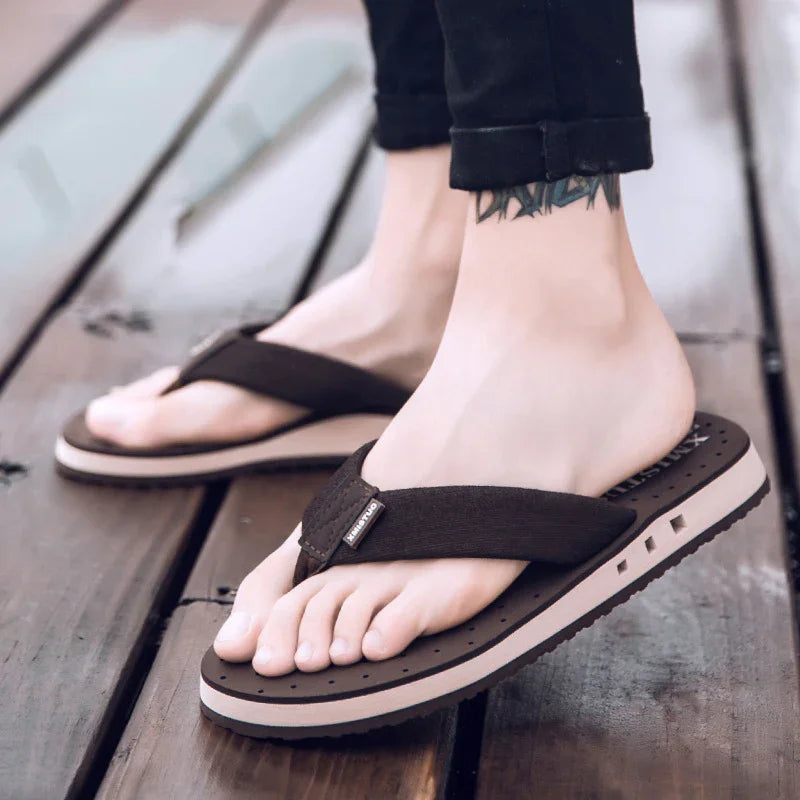 Close-up of feet wearing black and beige foam flip flop sandals on wooden floor