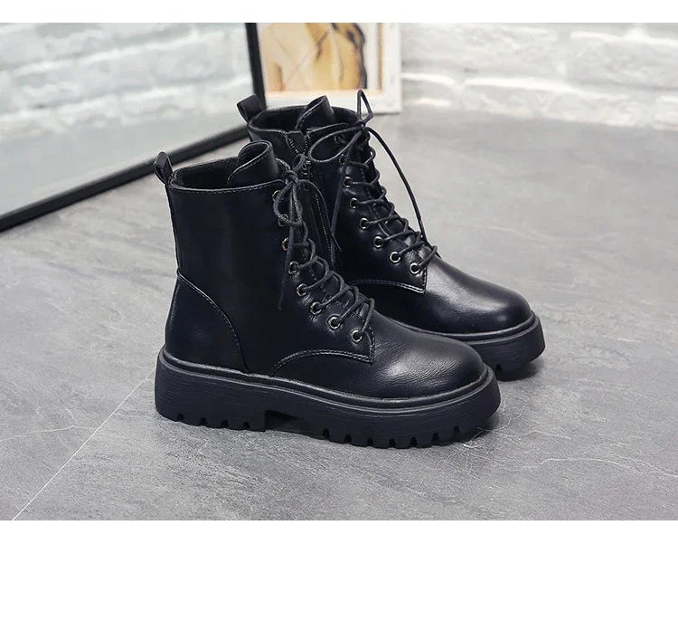 Pair of black leather combat boots with lace-up front and chunky soles on gray floor