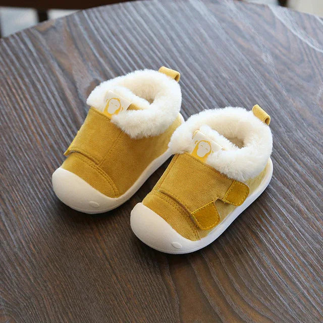 Yellow toddler winter shoes with white fur lining and soft sole on wooden surface