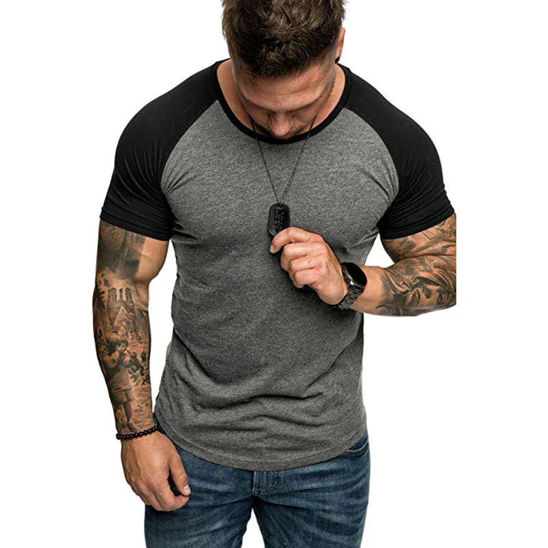Muscular man wearing grey and black raglan sleeve t-shirt with tattoos, blue jeans, and accessories