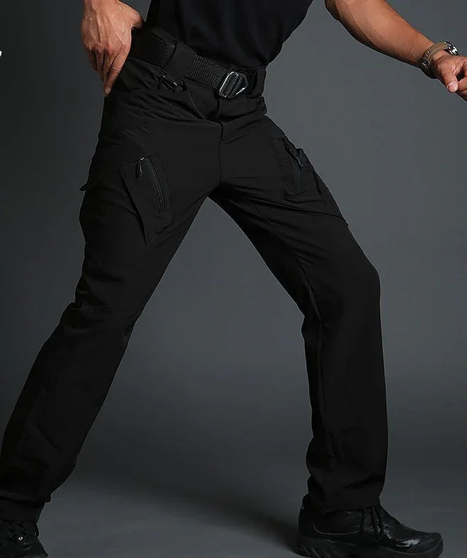 Man wearing black tactical cargo pants with multiple zippered pockets and a black belt