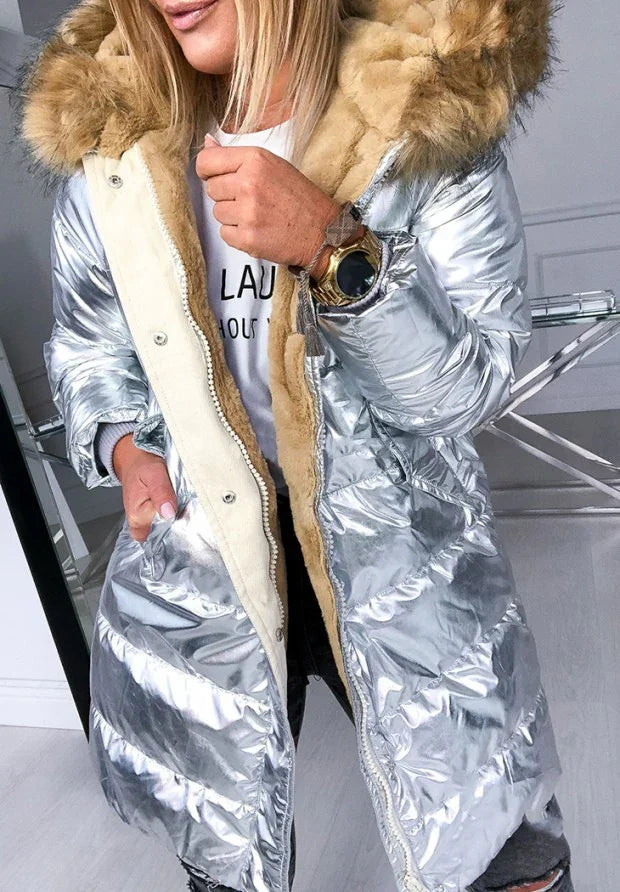 Woman wearing shiny silver puffer coat with beige faux fur hood and plush lining, casual indoor setting
