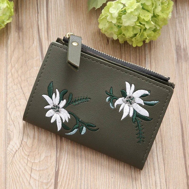 Green leather wallet with white floral embroidery and zipper, on wooden surface with green hydrangea flowers