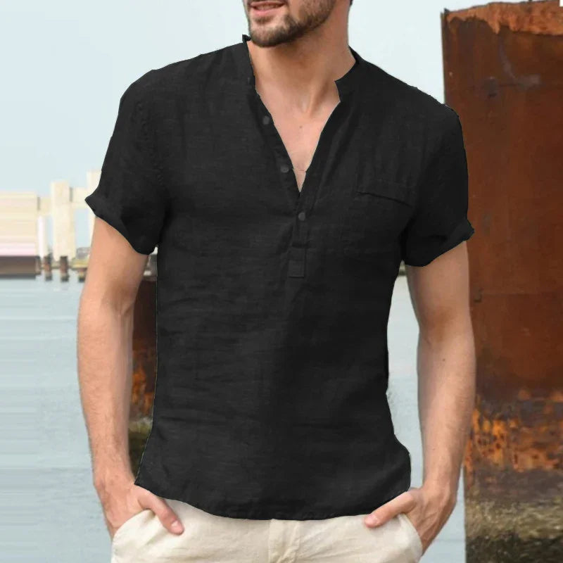 Man wearing casual black short-sleeve henley shirt with rolled cuffs near waterfront and rusted metal structure