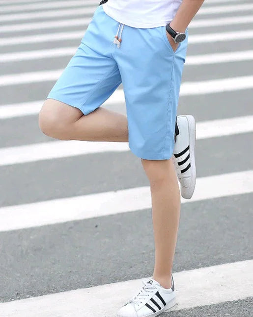 Man wearing light blue drawstring shorts and white Adidas sneakers standing on a crosswalk