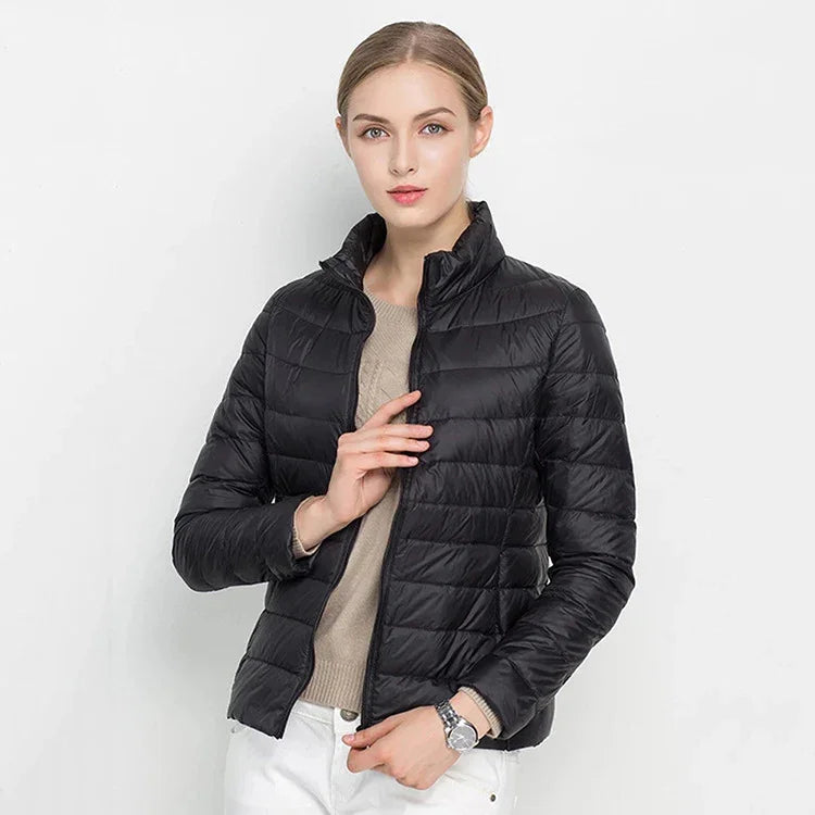 Young woman wearing black quilted puffer jacket with beige sweater and white pants on white background