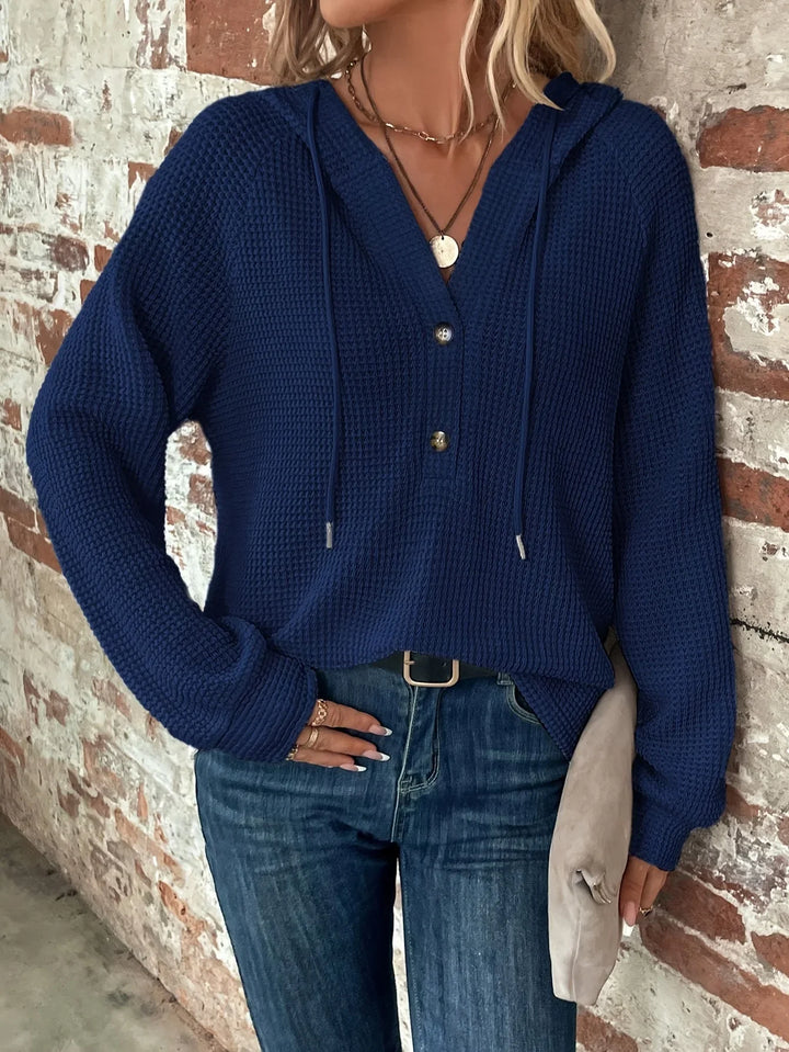 Woman wearing navy blue waffle knit hooded sweater with buttons, paired with blue jeans and accessories