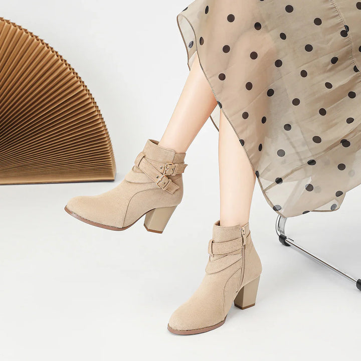 Beige suede ankle boots with buckled straps worn with a sheer polka dot skirt on white background