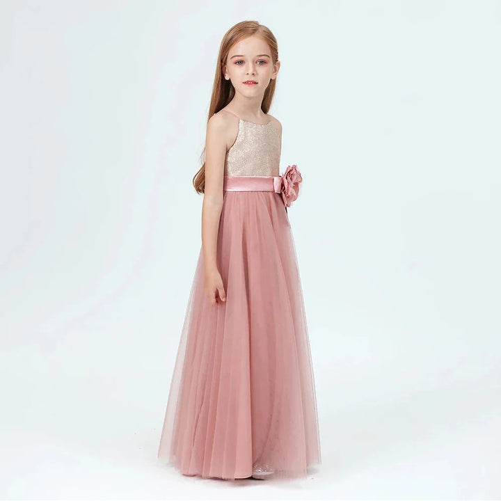 Young girl wearing a long pink tulle dress with a floral waist belt against a white background