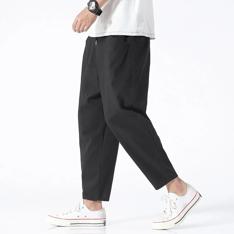 Person wearing black casual pants with white sneakers and a black wristwatch on a white background