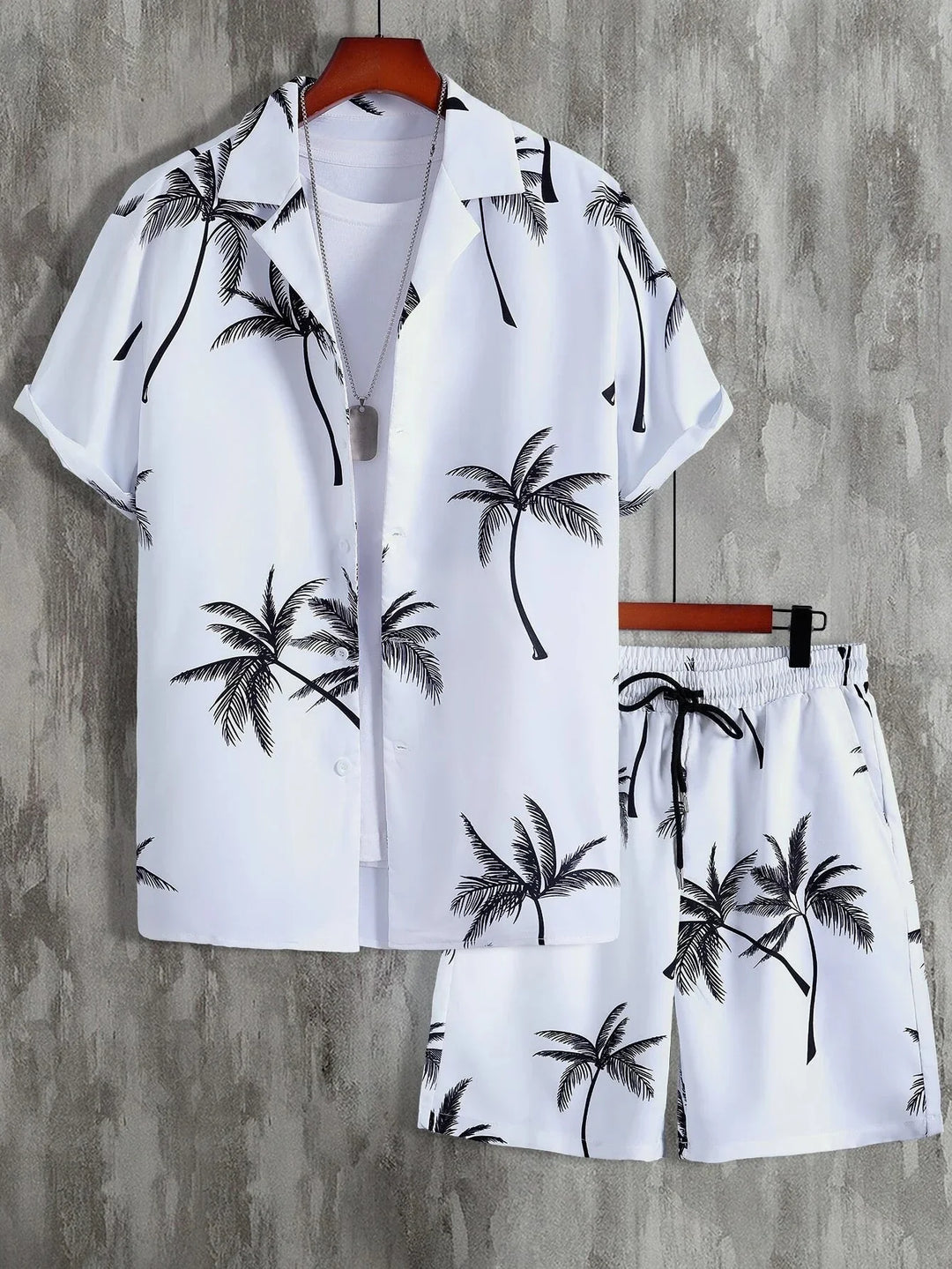 White casual shirt and shorts set with black palm tree print, displayed on hangers with a silver necklace