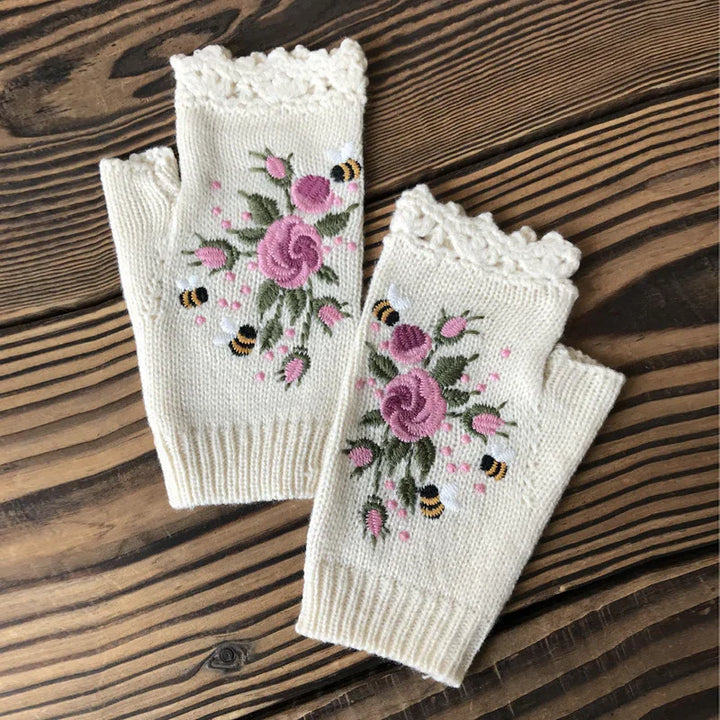 Cream knit fingerless gloves with pink embroidered roses and bees on a wooden surface