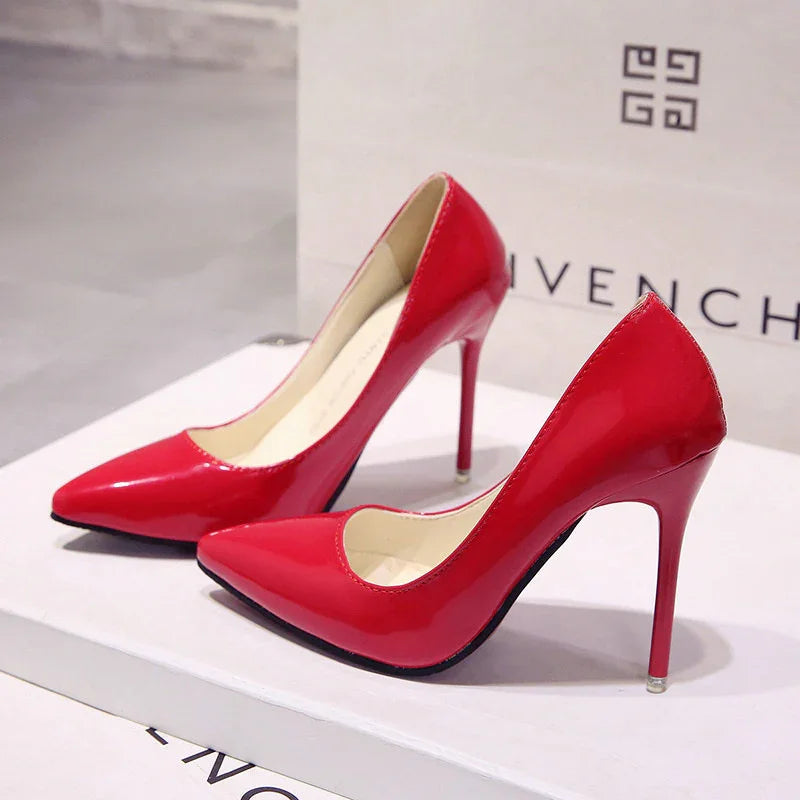 Shiny red patent leather high heel stiletto shoes on white surface with Givenchy bag background