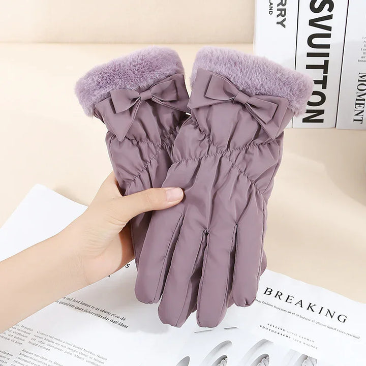 Hand holding purple winter gloves with faux fur cuffs and decorative bows