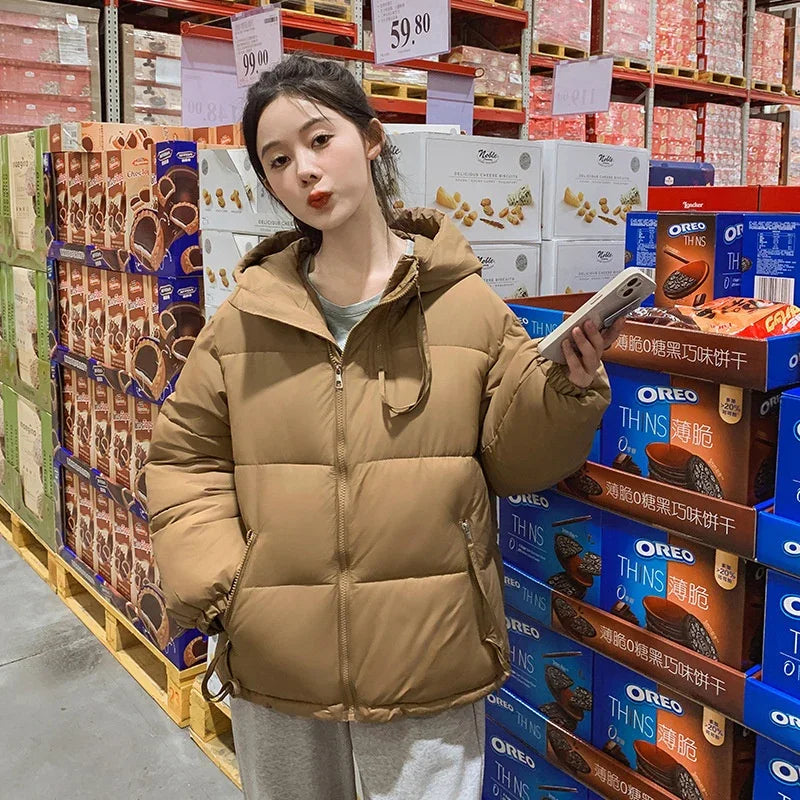 Young woman in brown puffer jacket shopping in aisle with Oreo and snack boxes in wholesale store
