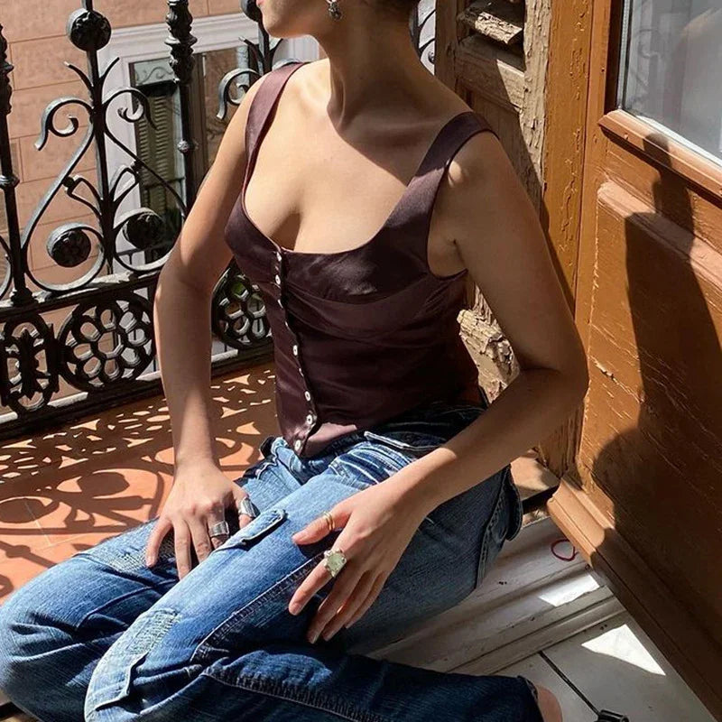 Woman wearing brown buttoned tank top and blue jeans sitting on a sunny balcony with ornate black iron railing