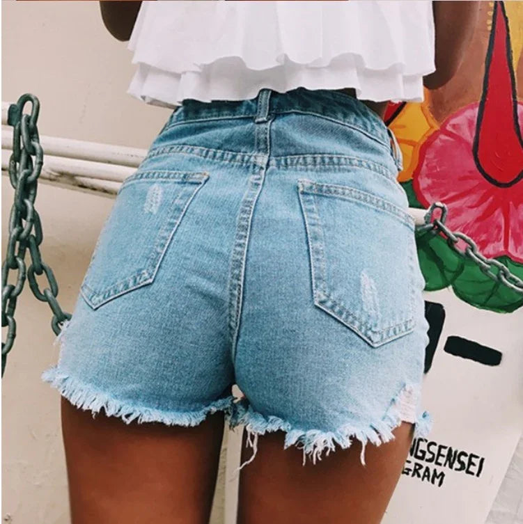 Back view of person wearing high-waisted distressed denim shorts with frayed hems and white layered top