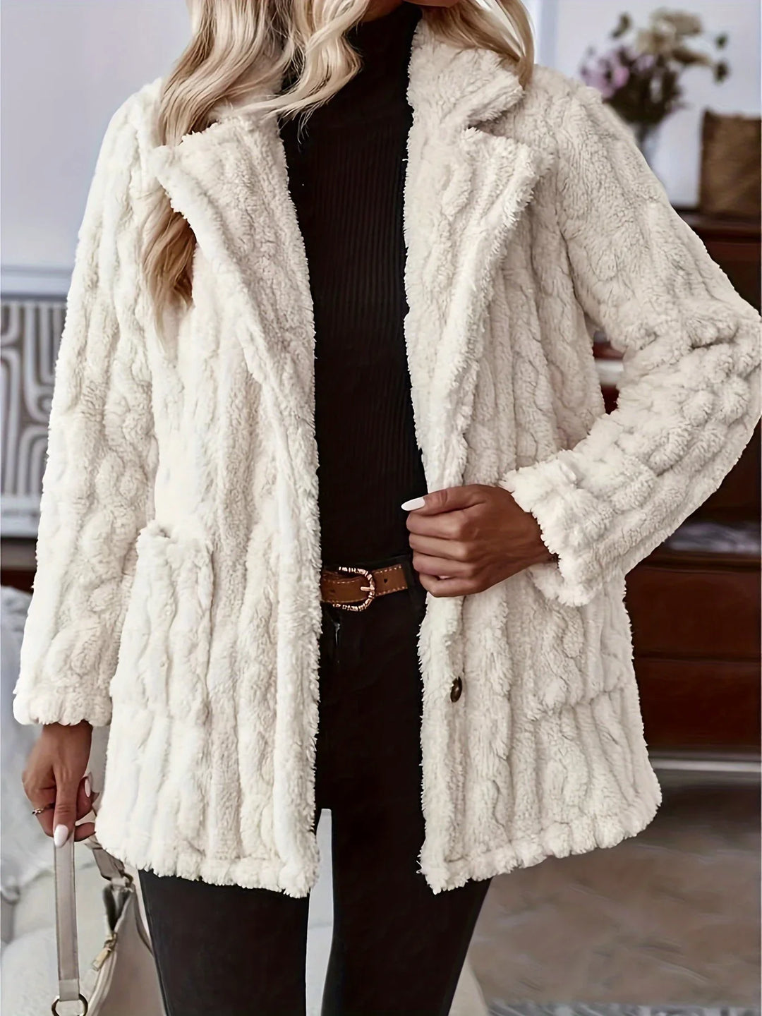 Woman wearing cream cable knit sherpa fleece coat with black turtleneck and black pants
