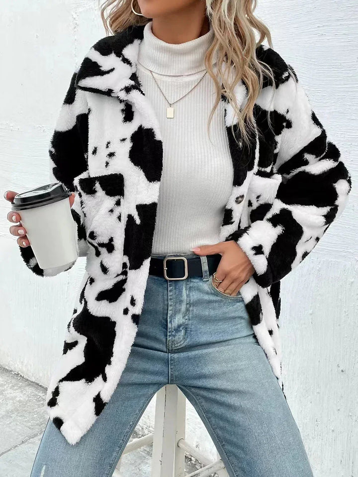 Woman wearing black and white cow print fur jacket, white turtleneck, blue jeans, holding coffee cup