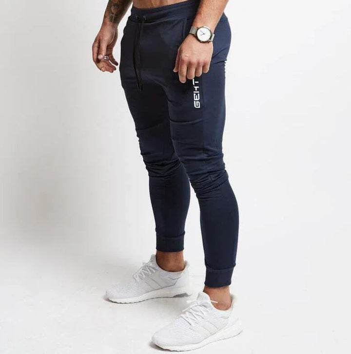 Man wearing navy blue slim-fit jogger pants with white text and white athletic sneakers on white background