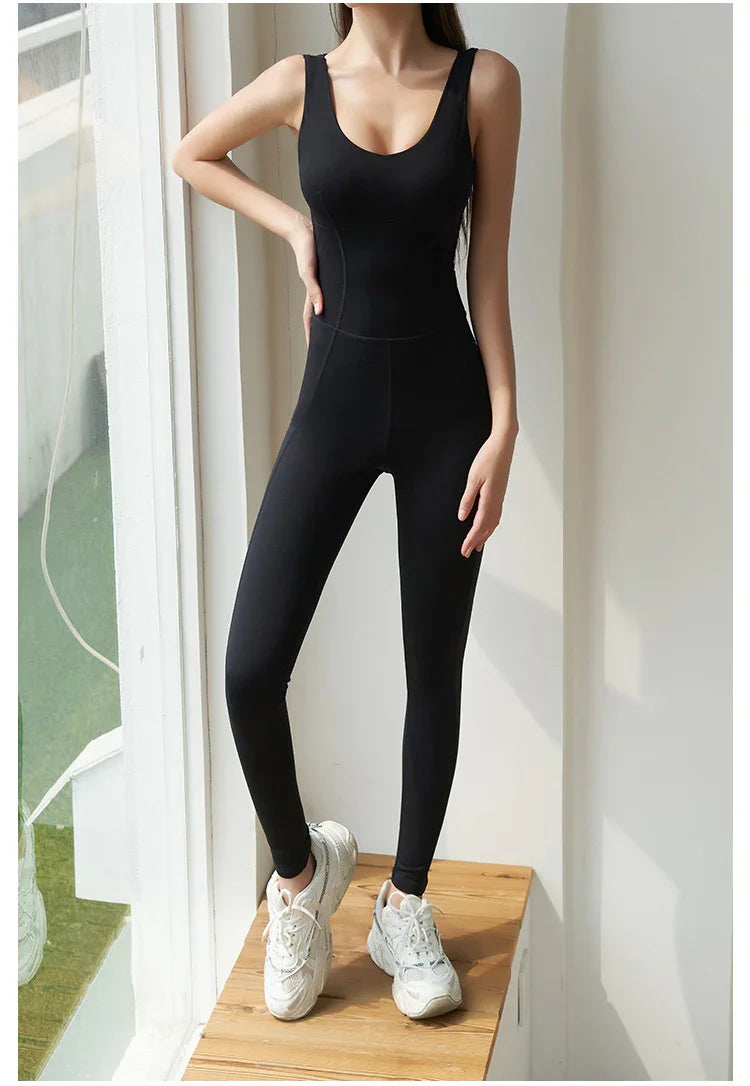 Woman in black fitted sleeveless jumpsuit and white sneakers standing on wooden platform by window