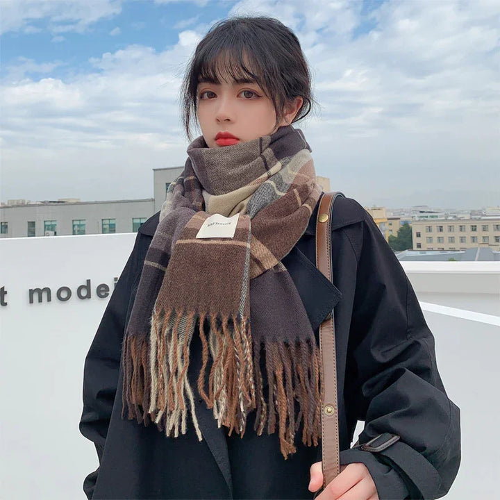 Young woman wearing a large brown plaid scarf and black coat outdoors against a cloudy sky