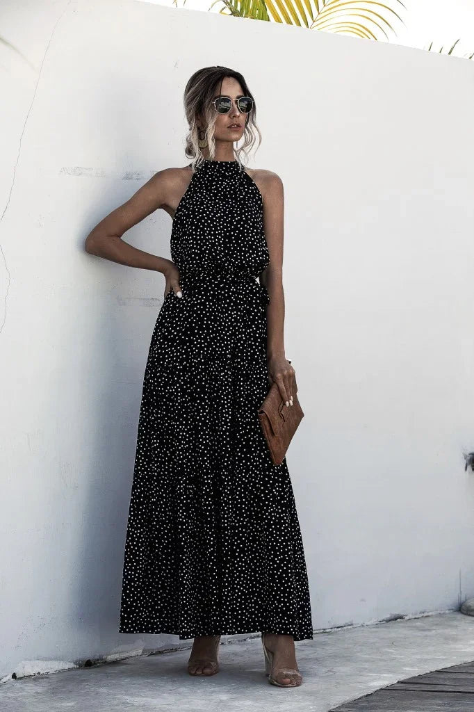 Fashionable woman in black polka dot halter maxi dress, sunglasses, and holding brown clutch outdoors