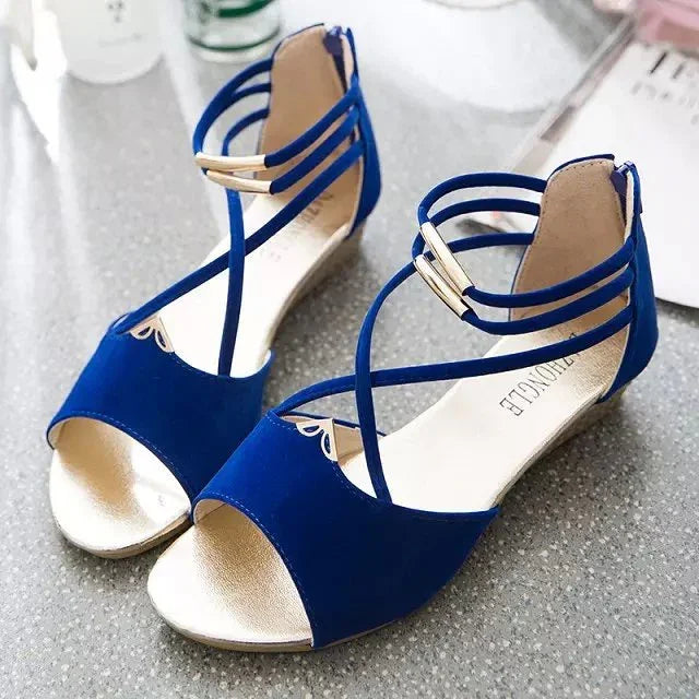 Pair of elegant blue and gold open-toe flat sandals with ankle straps on a gray surface