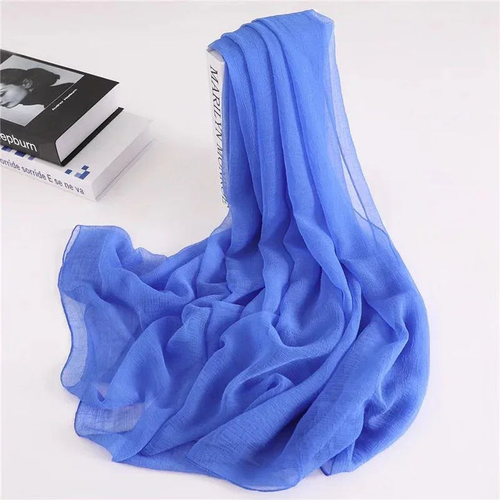 Soft blue sheer scarf draped over a book with two stacked books on a white background