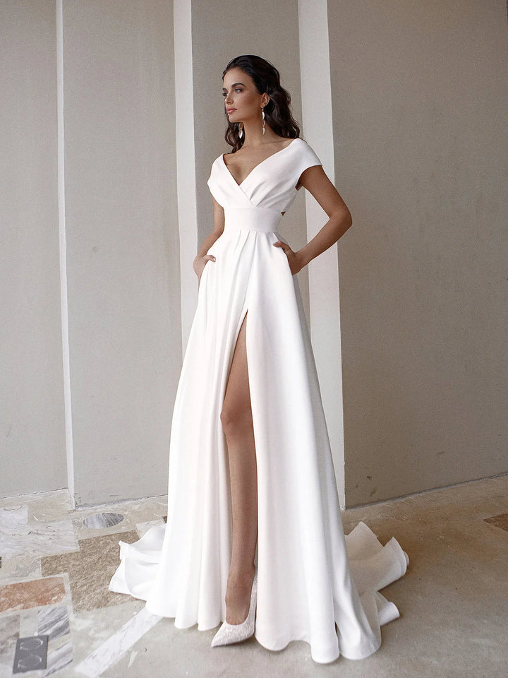 Elegant woman modeling white wedding dress with deep V-neck and thigh-high slit indoors