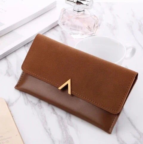 Brown leather and suede wallet with gold accent on marble surface, white cup and perfume bottle nearby
