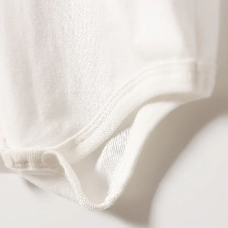 Close-up of white cotton baby bodysuit with snap buttons on soft fabric