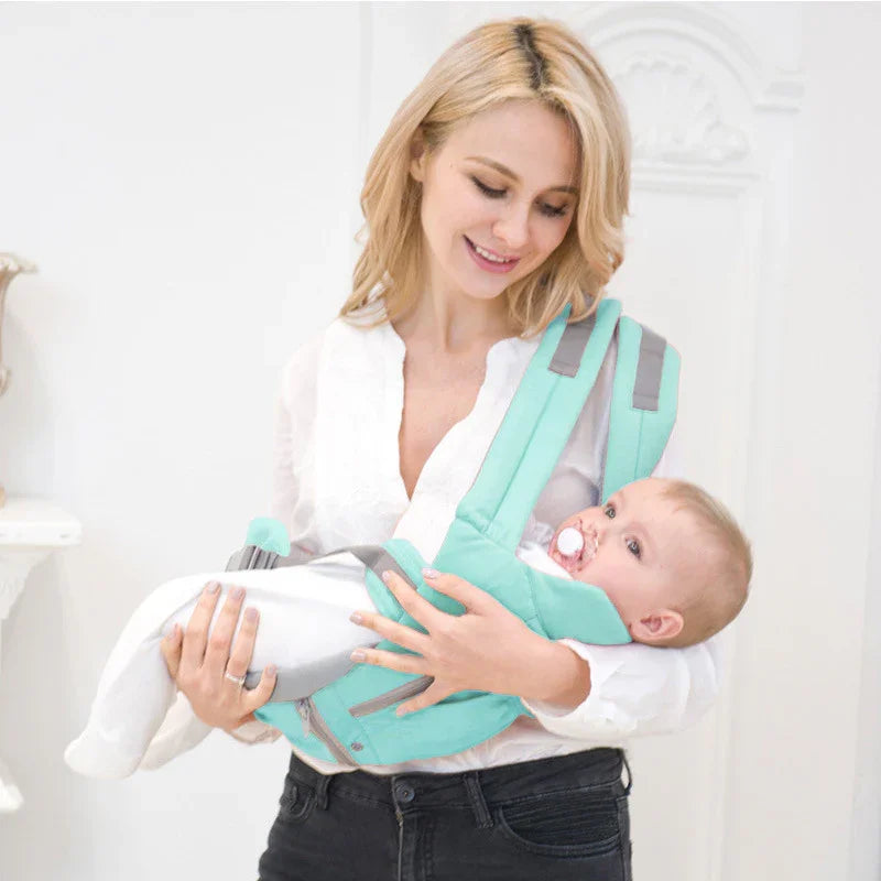 Smiling mother holding baby in turquoise and gray baby carrier in bright white room