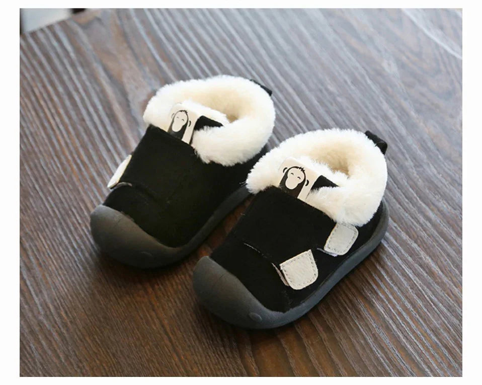 Black toddler shoes with white fleece lining and monkey cartoon tag on wooden floor