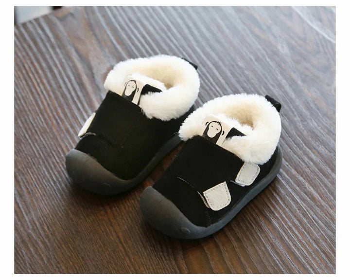 Black toddler shoes with white fleece lining and monkey cartoon tag on wooden floor
