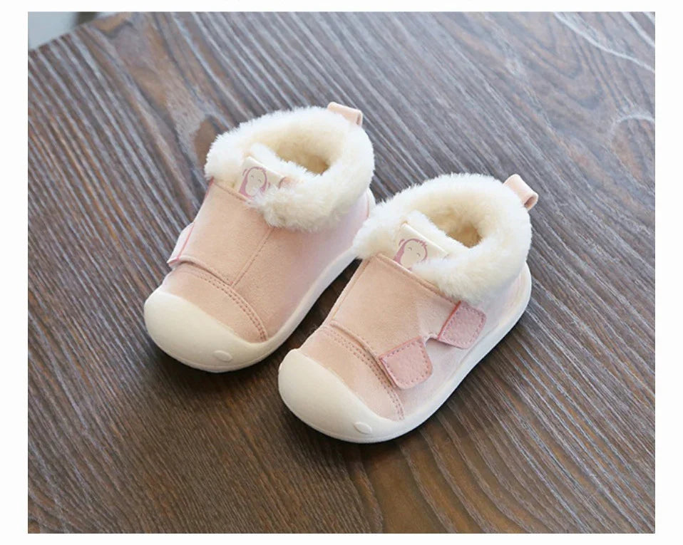 Pink baby shoes with white fur lining and soft soles on wooden floor
