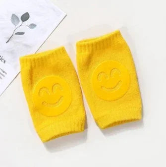 Yellow knit wrist warmers with smiling face design on a white surface with a leaf illustration