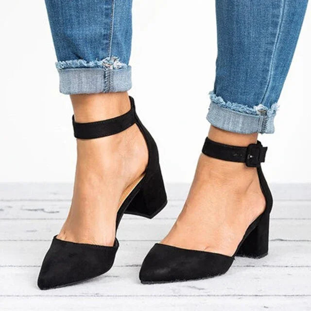 Black suede block heel shoes with ankle straps worn with frayed cuff blue jeans on white wooden floor