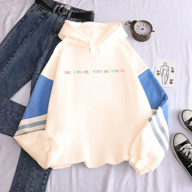 White hoodie with blue sleeves and colorful text 'Treat People With Kindness' paired with blue jeans and black sneakers
