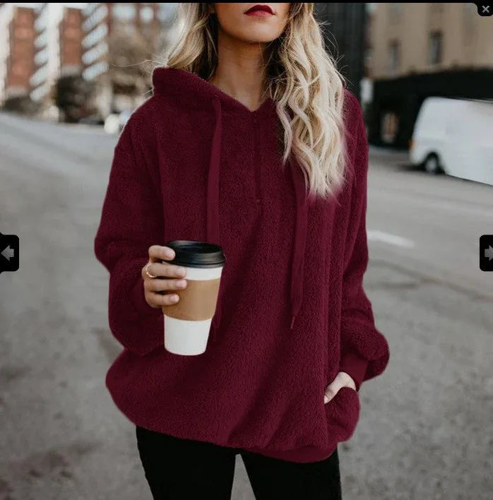 Woman wearing cozy burgundy hoodie holding coffee cup on urban street with buildings in background