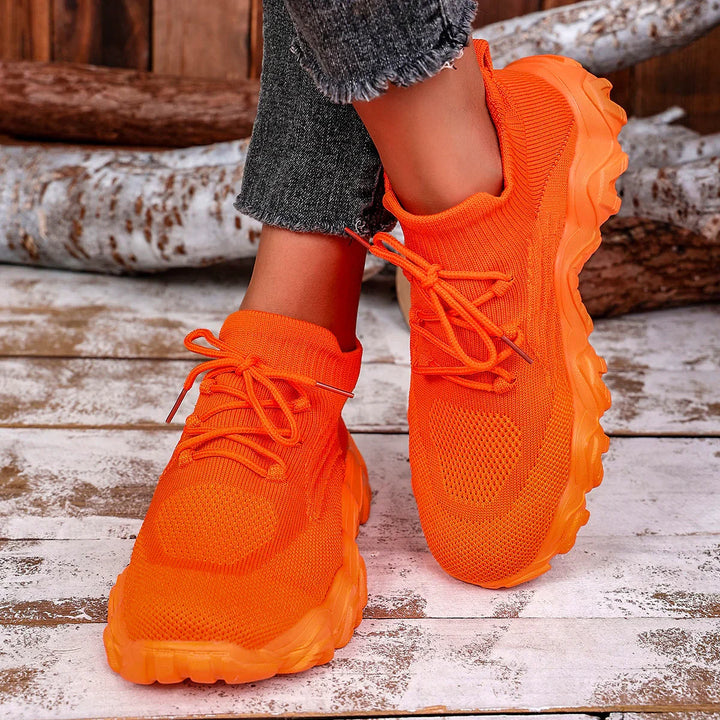 Bright orange knit sneakers with chunky sole worn with frayed black jeans on rustic wooden floor