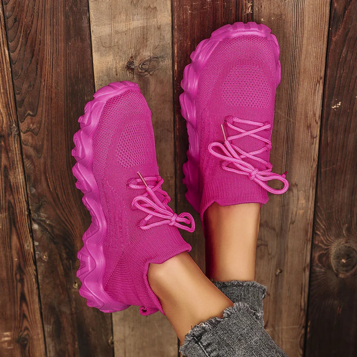 Pink chunky sole knit sneakers with laces worn with gray frayed jeans on wooden floor