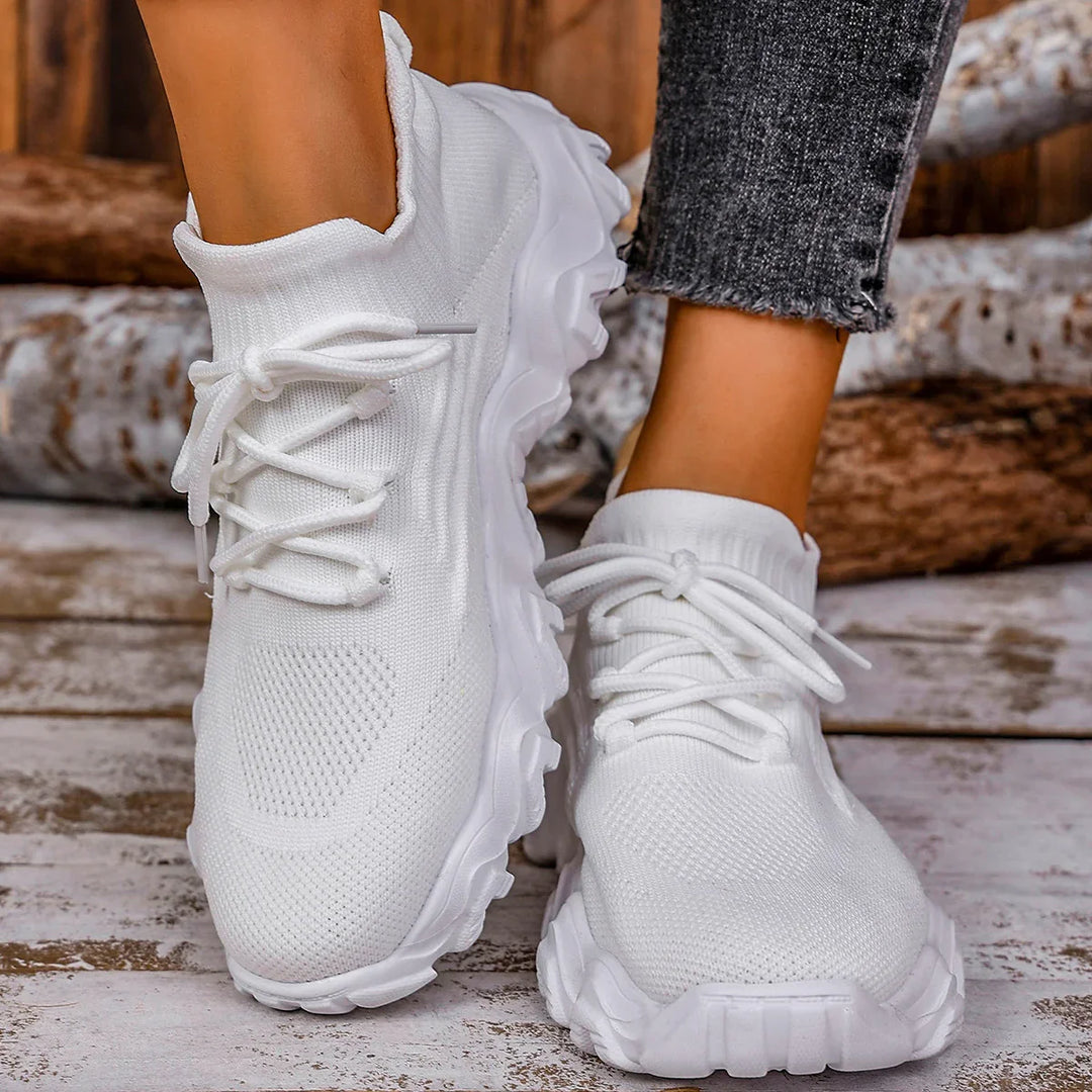 Close-up of white knitted athletic sneakers with chunky soles worn with black ripped jeans on wooden floor