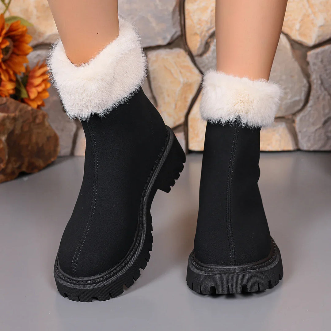 Black winter boots with white fur cuffs and chunky treaded soles on a stone background