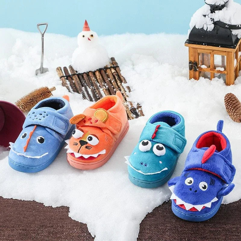 Four colorful toddler slippers with animal faces on snowy surface, winter decor including snowman and lantern