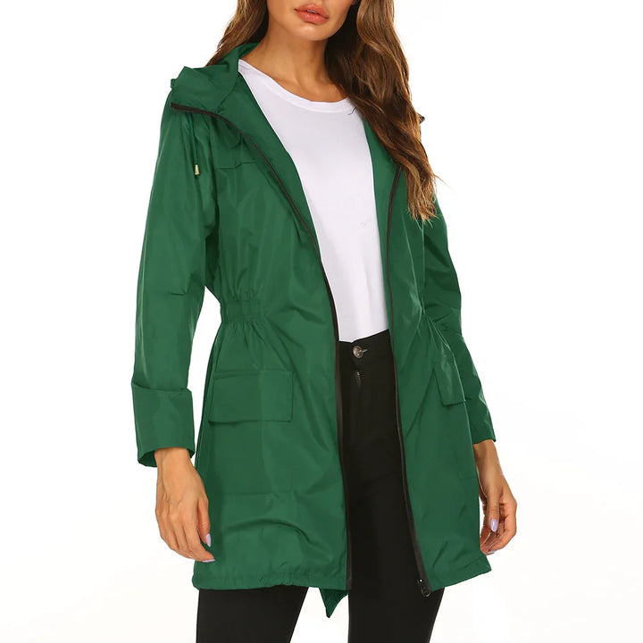 Woman wearing a green hooded raincoat with front pockets over a white top and black pants