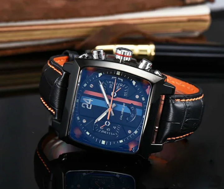 Black square chronograph watch with blue dial, orange stripes, and black leather strap featuring orange stitching