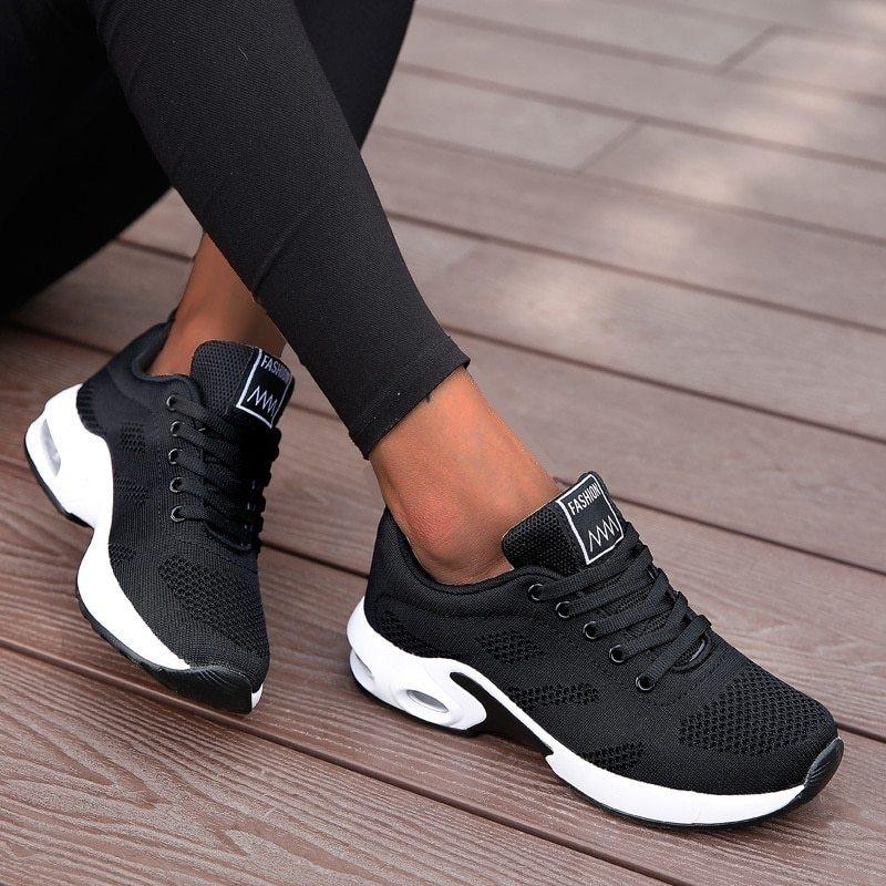 Black fashion sneakers with white sole and mesh design worn with black leggings on wooden floor