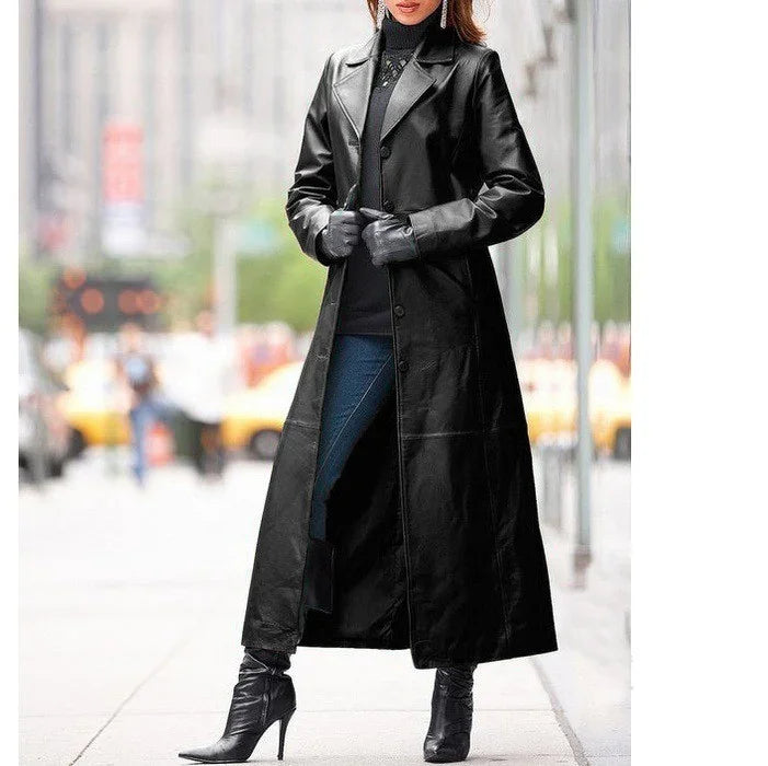Woman wearing a long black leather coat, black gloves, blue jeans, and black heeled boots on city street