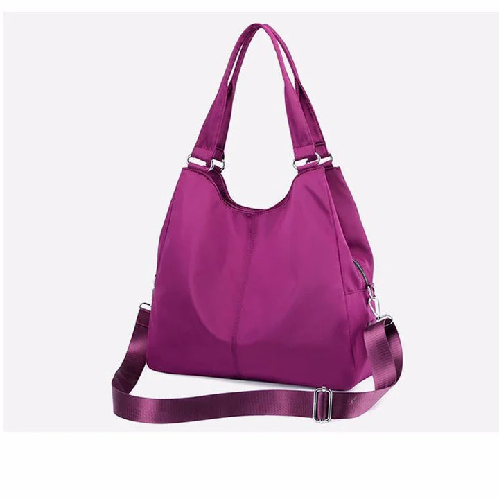 Purple nylon shoulder bag with dual handles and adjustable crossbody strap on white background